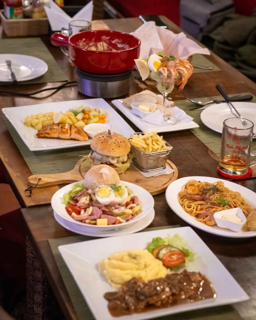 A diverse spread of Swiss and European dishes at TipTop Resto, including cheese fondue, pasta, salad, and signature entrees.