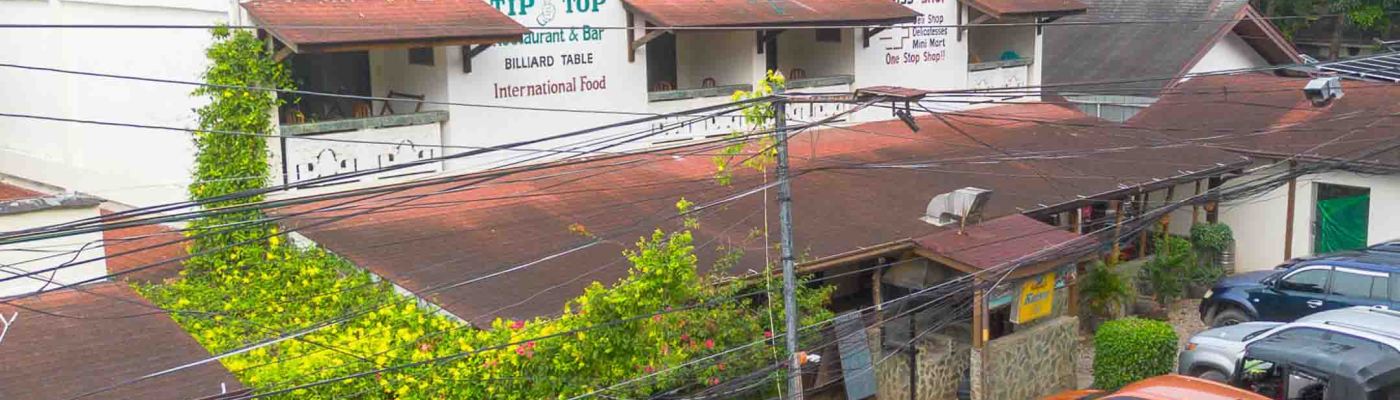 Wide exterior view of TipTop Hotel, Resto and Delishop in Panglao, Bohol, featuring the restaurant facade, outdoor terrace, and guest parking during the day.
