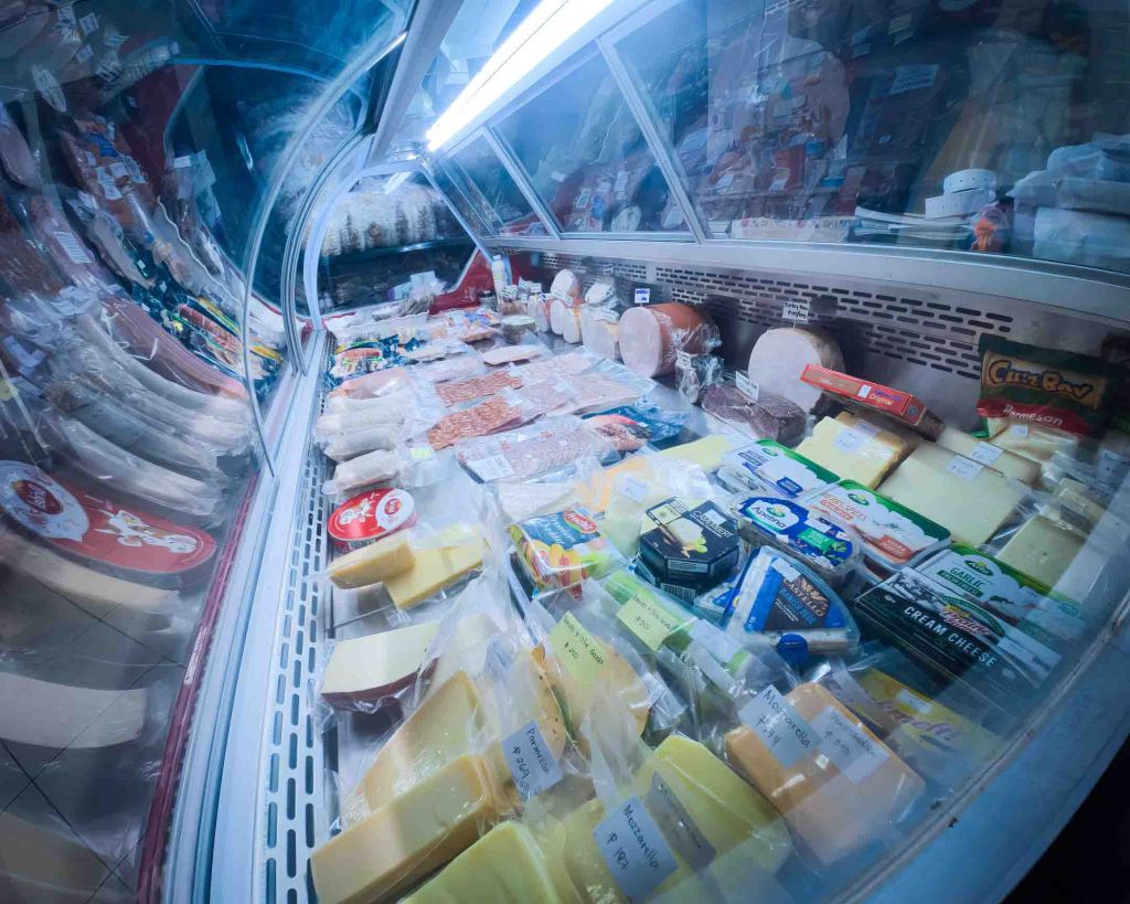 Refrigerated display at the TipTop Delishop filled with a wide selection of authentic European and Swiss cheeses.