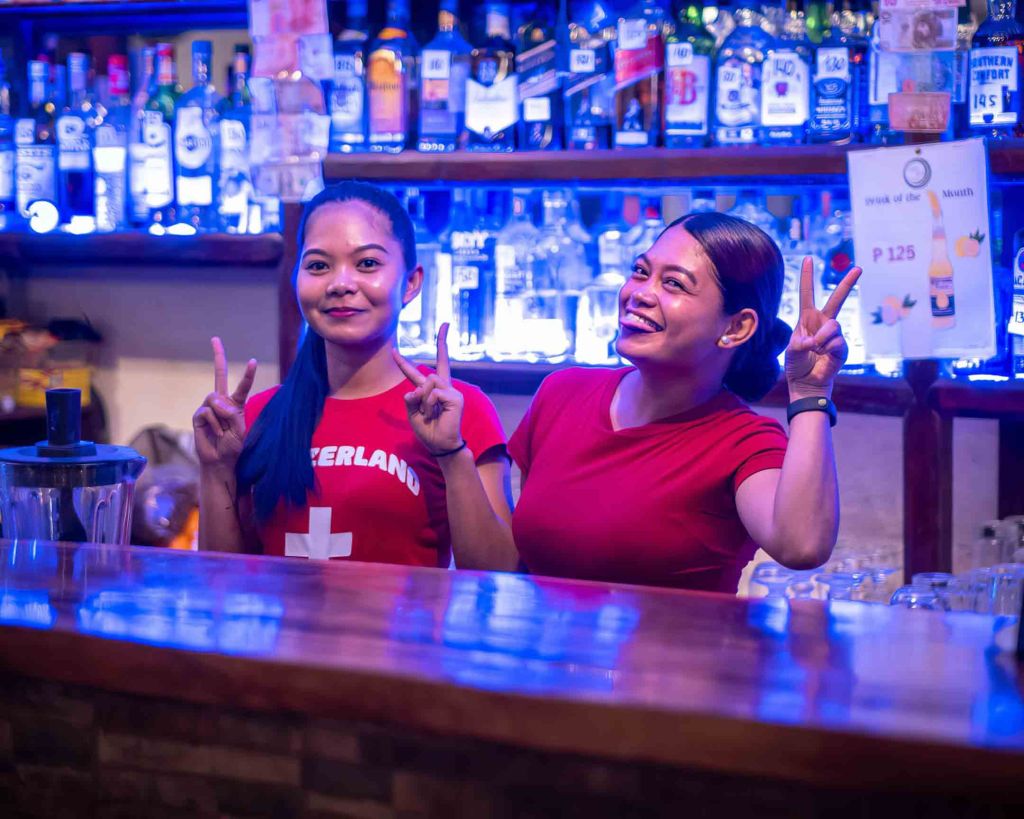 Cheerful bar staff at TipTop Resto wearing Switzerland-themed shirts, providing a welcoming environment for the local community.